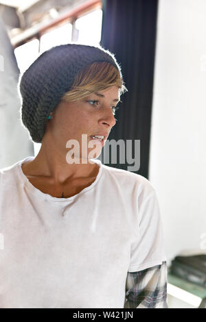 Jeune femme avec un chapeau et des cheveux plus courts en disant quelque chose et regarder ailleurs dans une chambre Banque D'Images