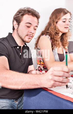 Jeune homme et d'une femme écrivant des lettres à l'aide d'un pinceau holding verticalement sur le papier comme lors de l'écriture chinoise Banque D'Images