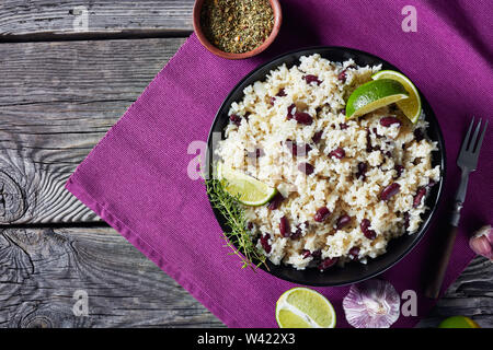 Close-up of Jamaican Riz et haricots rouges cuits avec du lait de coco assaisonné d'ail, oignons et épices créoles dans un bol sur une table en bois rustique, vie Banque D'Images
