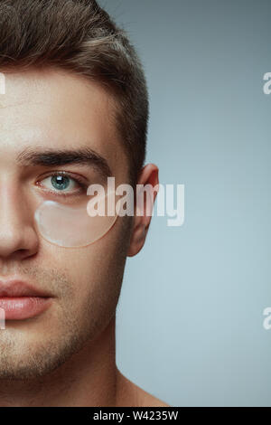 Close-up portrait of young man isolé sur fond studio gris. Visage masculin avec patches collagène sous les yeux. Concept de la santé des hommes et de la beauté, les soins de beauté, soins du corps et de la peau. Anti-vieillissement. Banque D'Images