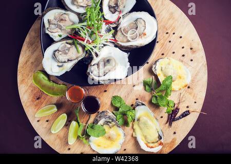 Les huîtres ouvertes sur la glace fruits de mer frais et cuits servis avec la sauce sur plateau en bois Banque D'Images