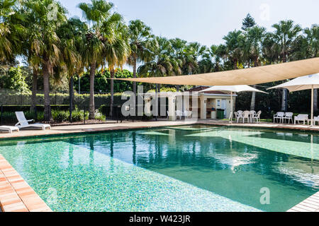 Vue d'une piscine dotée d'une ombre sur une section, ainsi que des palmiers à l'arrière goutte Banque D'Images