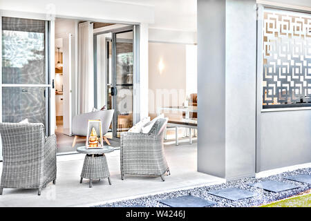 Vue sur la façade d'une maison moderne avec des chaises en rotin ou en plastique sur le plancher de tuiles à côté de l'entrée de porte de la maison, il y a une fantaisie articles comme un Banque D'Images