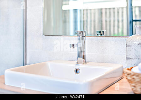 Robinet évier blanc et argent fermer jusqu'à côté d'un miroir d'une salle de bain moderne, endroit très propre avec la foudre parfait, les murs sont carrelés colorés aussi. Banque D'Images