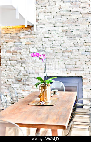 Plante à fleurs de fantaisie dans un vase avec des fleurs d'orchidées, sur une vieille table en bois avec des chaises dans un mur de pierre prix Banque D'Images