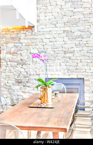 Plante à fleurs de fantaisie dans un vase avec des fleurs d'orchidées, sur une vieille table en bois avec des chaises dans un mur de pierre prix Banque D'Images