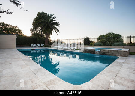 L'eau de luxe vue sur la piscine avec un carrelage sol avec des chaises et une petite fontaine, il y a une clôture à proximité d'arbres Banque D'Images