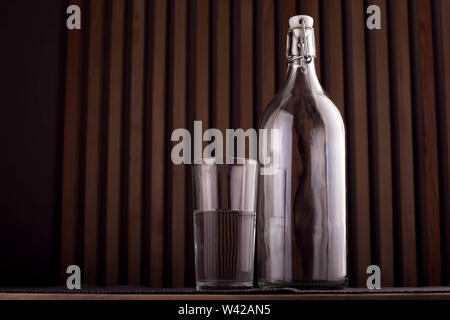 Une bouteille vide et verre avec de l'eau sur fond de bois. Banque D'Images