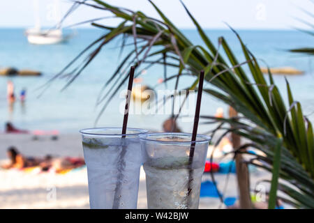 Deux cocktails glacés pailles avec happy hour au temps sur une plage tropicale Banque D'Images