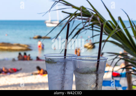 Deux cocktails glacés pailles avec happy hour au temps sur une plage tropicale Banque D'Images