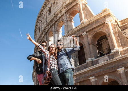 Trois jeunes amis heureux touristes debout devant coliseumin rome posant pour des photos s'amusant Banque D'Images