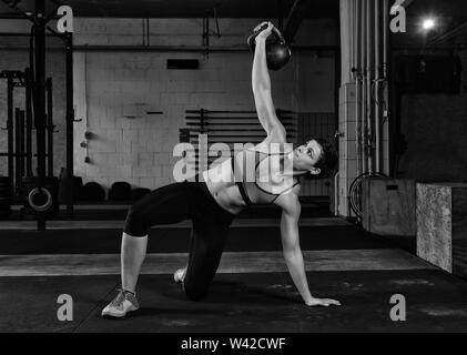 Une femme aux cheveux courts avec fait abs fort poids de levage avec un kettlebell dans une salle de sport. Obtenez jusqu'turc d'exercice. Noir et blanc. Banque D'Images