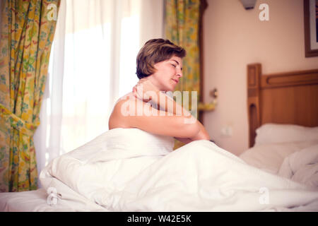 Jeune femme aux cheveux courts assise sur le lit avec douleur dans le cou. Les gens, les soins de santé et de style de concept Banque D'Images