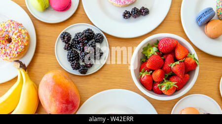 Petit-déjeuner de fruits, banane, fraise, mûre, de mangue et de beignets colorés et ses macarons sur le bois. Banque D'Images