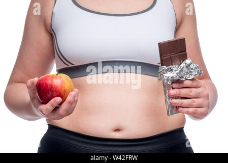 Grosse femme fait un choix difficile entre une pomme et chocolat, dans le cadre d'un close-up belly Banque D'Images