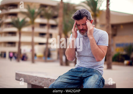 Man having a headache assis sur un banc à l'extérieur. Les gens, les soins de santé et la médecine concept Banque D'Images