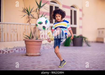 Petit garçon aux cheveux bouclés avec ballon de soccer extérieur. Les enfants et de divertissement concept Banque D'Images