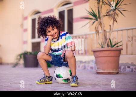 Petit garçon aux cheveux bouclés avec ballon de soccer extérieur. Les enfants et de divertissement concept Banque D'Images
