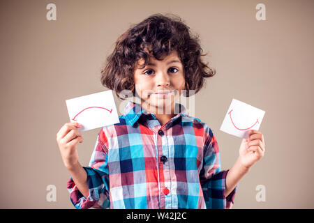 Kid boy sélectionnez entre les expressions positives et négatives. Les enfants et les émotions concept Banque D'Images