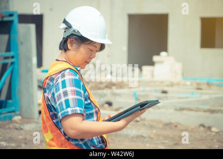 Les femmes asiatiques engineering est titulaire d'une tablette pour une utilisation dans l'inspection des chantiers de construction pour plus de précision et en conformité avec le plan. Concept de l'égalité de Banque D'Images