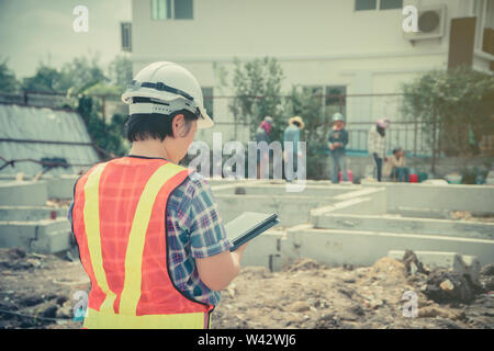 Les femmes asiatiques engineering est titulaire d'une tablette pour une utilisation dans l'inspection des chantiers de construction pour plus de précision et en conformité avec le plan. Concept de l'égalité de Banque D'Images