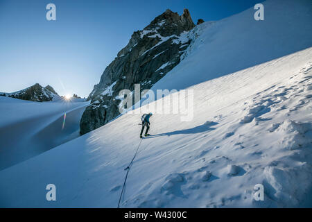 Un alpiniste aborde une pente de neige raide comme le soleil de l'horizon des crêtes Banque D'Images