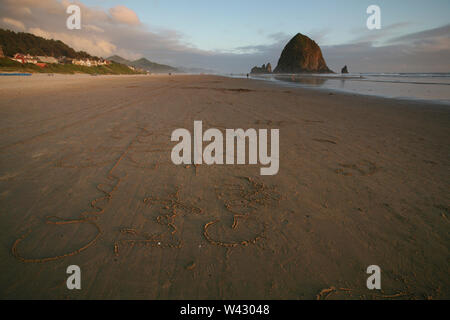 L'écriture de sable sur Cannon Beach, Haystack rock avec en arrière-plan Banque D'Images