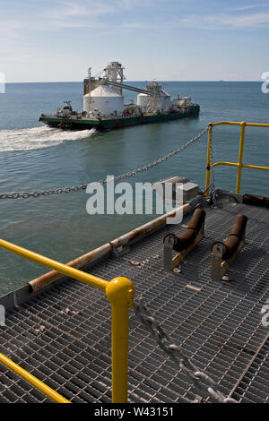 Exploitation minière, gestion et transport des sables bitumineux en titane. Barge quittant le port pour décharger le produit dans l'OGV en mer et montrant l'infrastructure de la jetée . Banque D'Images