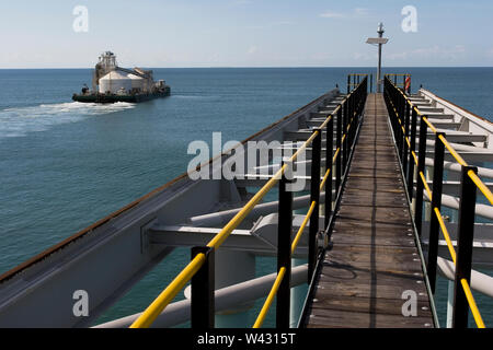 Exploitation minière, gestion et transport des sables bitumineux en titane. Barge quittant le port pour décharger le produit dans l'OGV en mer et montrant l'infrastructure de la jetée . Banque D'Images