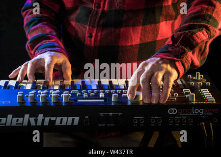 Un musicien jouant un synthétiseur analogique Elektron avec touches de bleu et orange éclairage de la scène. Banque D'Images