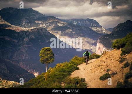 Un homme monte un vtt sur une piste de terre isolée dans les montagnes de l'Atlas. De hautes montagnes et rainclouds en arrière-plan.