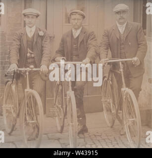 Vintage Carte postale photographique de trois hommes portant des chapeaux en tissu de la classe se tenait près de leurs cycles. Banque D'Images