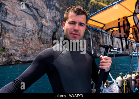Jeune homme de race blanche scuba diver action holding et la préparation de l'appareil photo de plongée voile plein d'équipement de plongée, l'île de Phi Phi, Thaïlande Banque D'Images