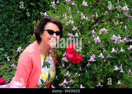 A young attractive woman smiling at camera à côté d'une rose rouge, UK - John Gollop Banque D'Images