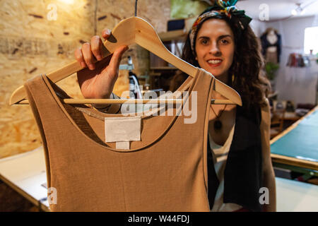 Un jeune éco-friendly clothes maker affiche nouveau gilet beige vêtement sur cintre en bois. Entrepreneur avec un produit. Banque D'Images