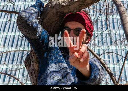 Un homme spirituel est situé dans un milieu urbain et donne à l'arbre V signer à l'appareil photo, le port de lunettes et d'un bandana rouge, est commerciale moderne vu dans backgrou Banque D'Images