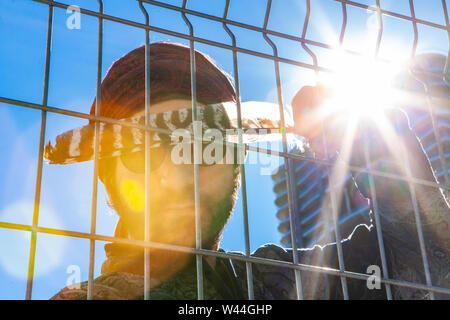 Un closeup portrait d'un homme spirituel tenant une plume d'aigle dans un environnement urbain, en portant des lunettes de soleil, derrière une clôture métallique et Banque D'Images