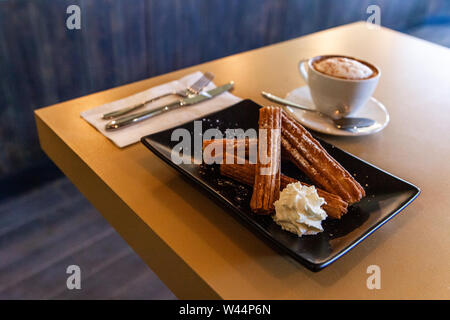 Un gros plan et high angle view of churros fraîchement préparé, servi avec de la crème fouettée et du cappuccino, un savoureux dessert composé de pâte frite. Banque D'Images