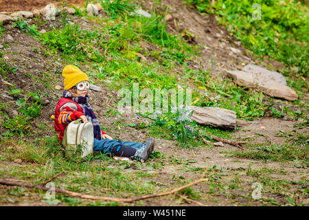 Une jeune fille est vu assis à l'extérieur tenant un sac à dos et portant des lunettes style minion jaune et chapeau, assise seule dans la nature avec copie espace à droite. Banque D'Images