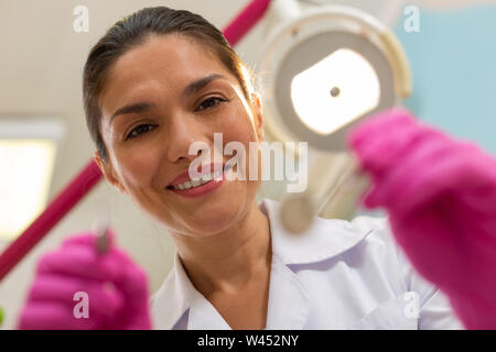 Dark-haired friendly Smiling female dentist holding instruments dentaires Banque D'Images