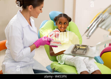 Smiling dark-haired femme dentiste à l'aide d'un modèle de soins dentaires Banque D'Images