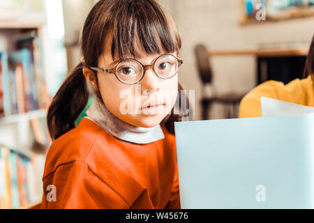 Cute little Girl with long bangs et lunettes holding open book Banque D'Images