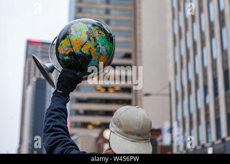 Un démonstrateur écologique est considérée close up de derrière, portant un chapeau et tenant un globe de la terre dans l'air au cours d'une manifestation, avec copie-espace sur la droite. Banque D'Images