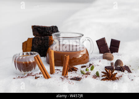 Un pichet de thé chai chaga fraîchement préparé est vu dans la neige, avec des ingrédients de la cannelle, l'anis étoilé et de chocolat noir, un verre canadien aromatiques Banque D'Images