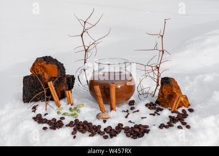 Le café et les fèves de cacao sont vus lying outdoors in snow, avec des bâtons de cannelle et décor naturel par un pichet rempli de chaga chai latte, une boisson brassée mystique Banque D'Images