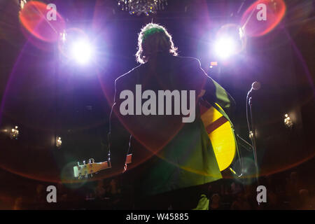 Un faible retour d'angle de vue éclairé d'un homme jouant de la guitare par un micro dans un bar avec musique, scène feux sont vu flou d'au-dessus comme il joue à un public. Banque D'Images
