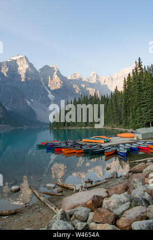 Des canots s'empilent sur les rives du lac Moraine avec des reflets dans le lac glaciaire des montagnes, derrière Banff, Alberta, Canada Banque D'Images