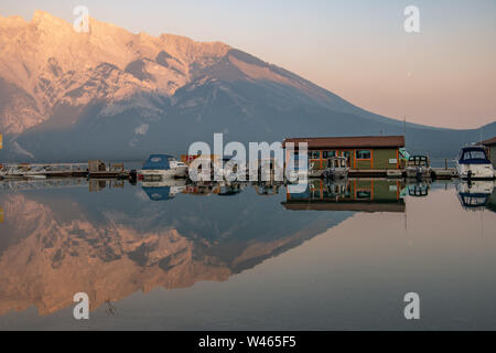 coucher de soleil sur la montagne derrière un lac STILL Minnewanka avec des reflets de bateaux Alberta, Canada Banque D'Images