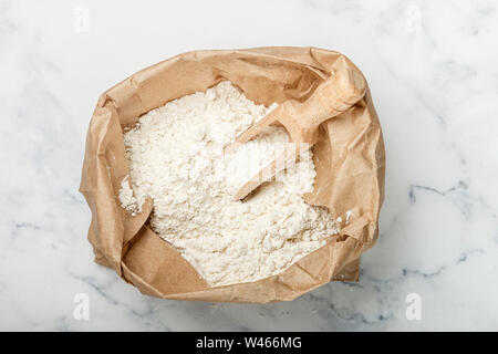 Farine de blé et d'un scoop en bois dans un sac en papier sur une table en marbre. boulangerie concept. Selective focus Banque D'Images