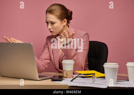 Jeune femme écarte ses mains travailler avec l'ordinateur portable qui posent sur fond rose Banque D'Images